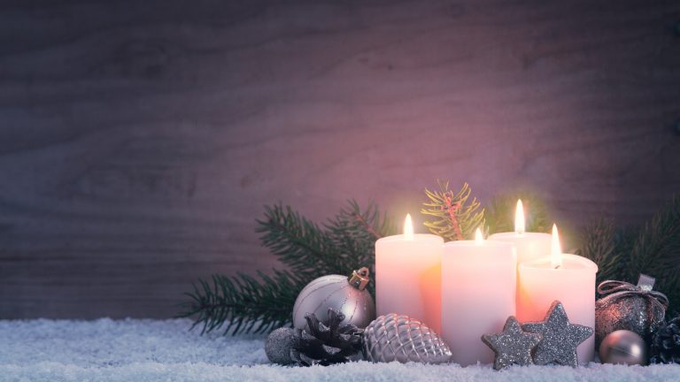 Das Bild zeigt einen Adventskranz mit angezündeten Kerzen.